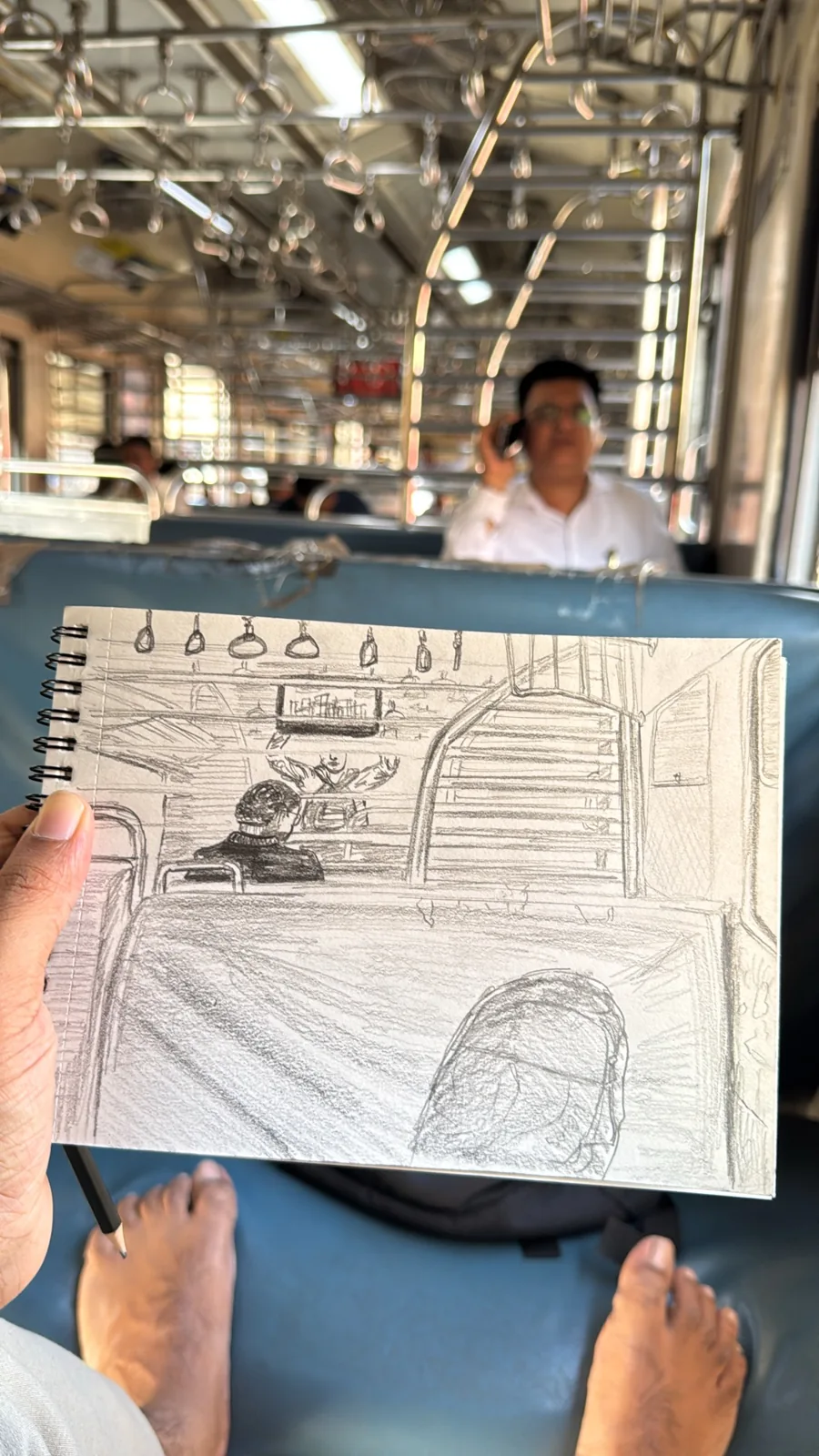 An open sketchbook held inside a train carriage