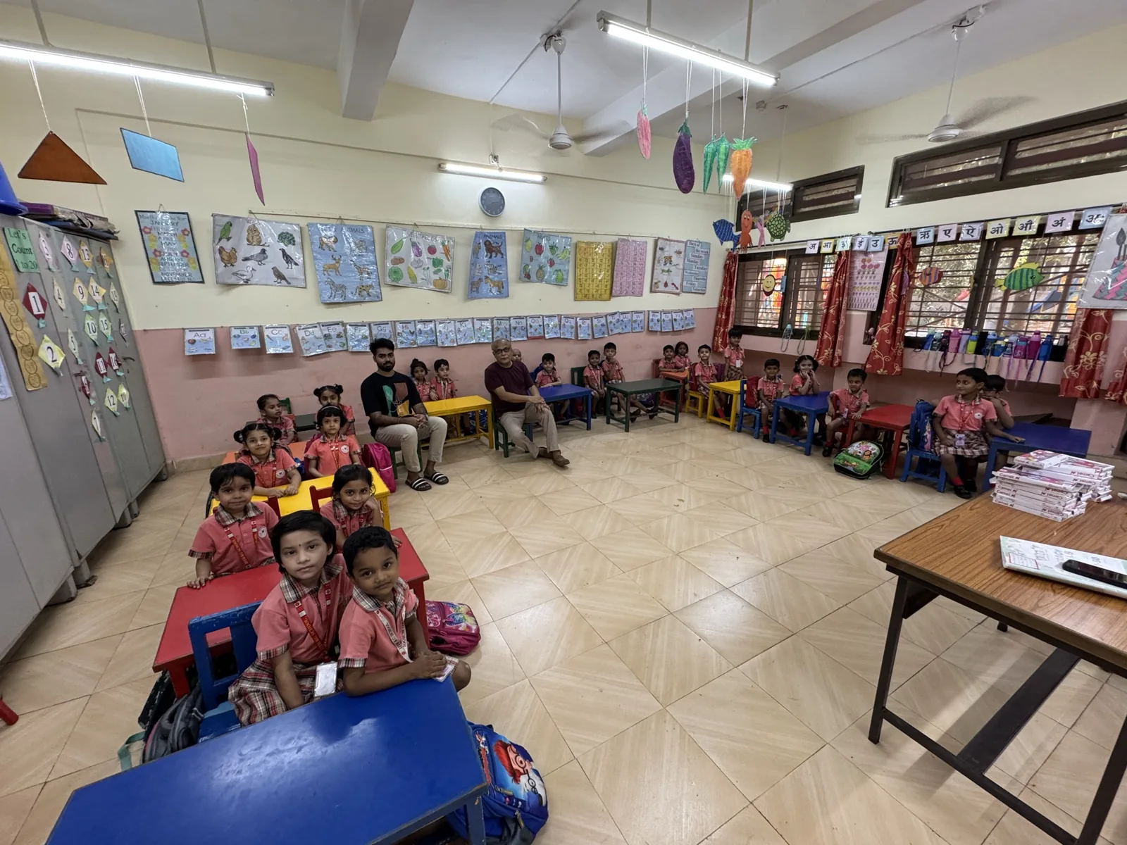 Children seated in a classroom with drawings displayed across the walls